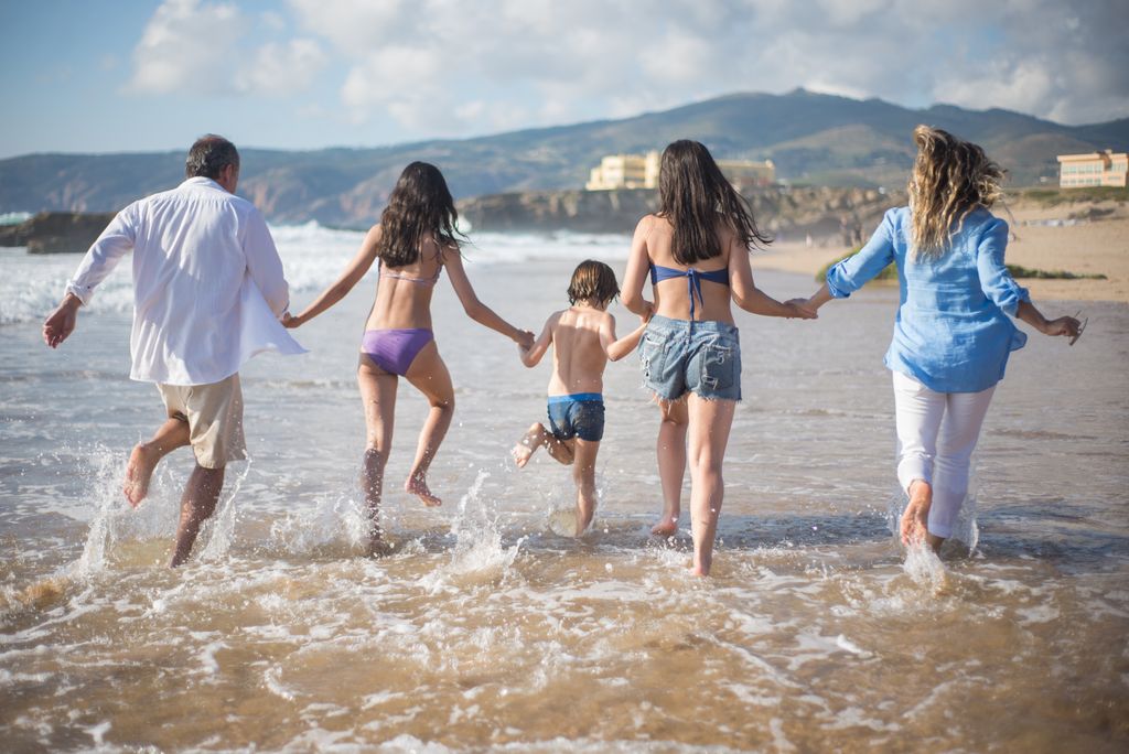 A family having fun running into the ocean on a sunny beach day in Portugal. Joyful and carefree moments.