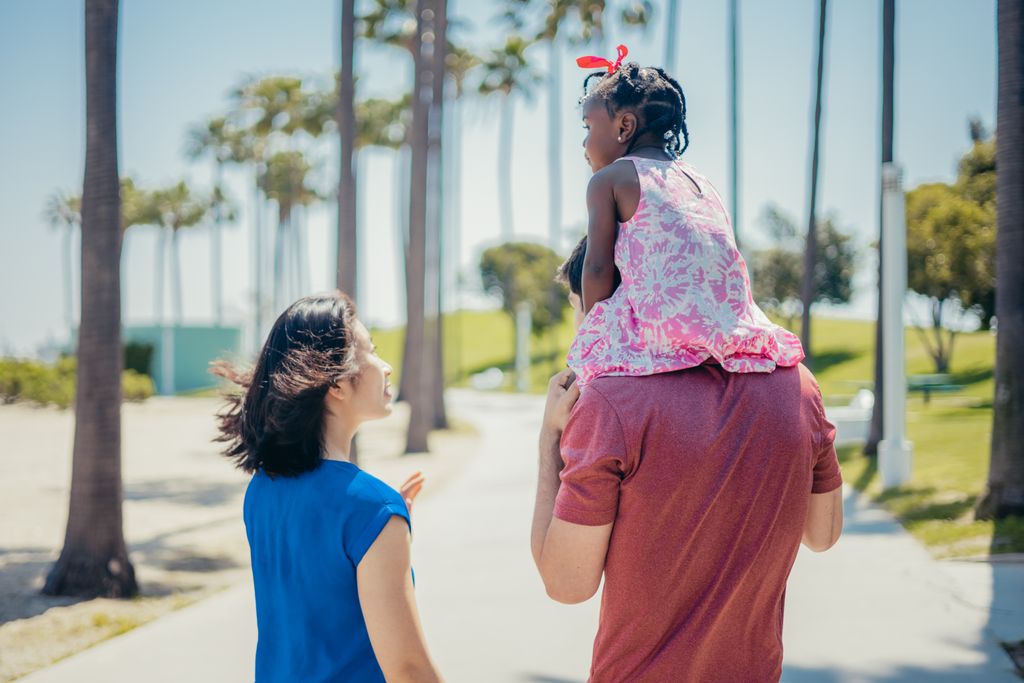 Child on shoulders with family in sunny park. Vibrant, joyful outdoor scene.