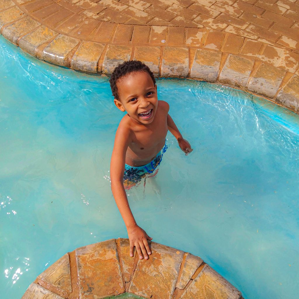 Happy child smiling and playing in a bright, clear swimming pool on a sunny day.
